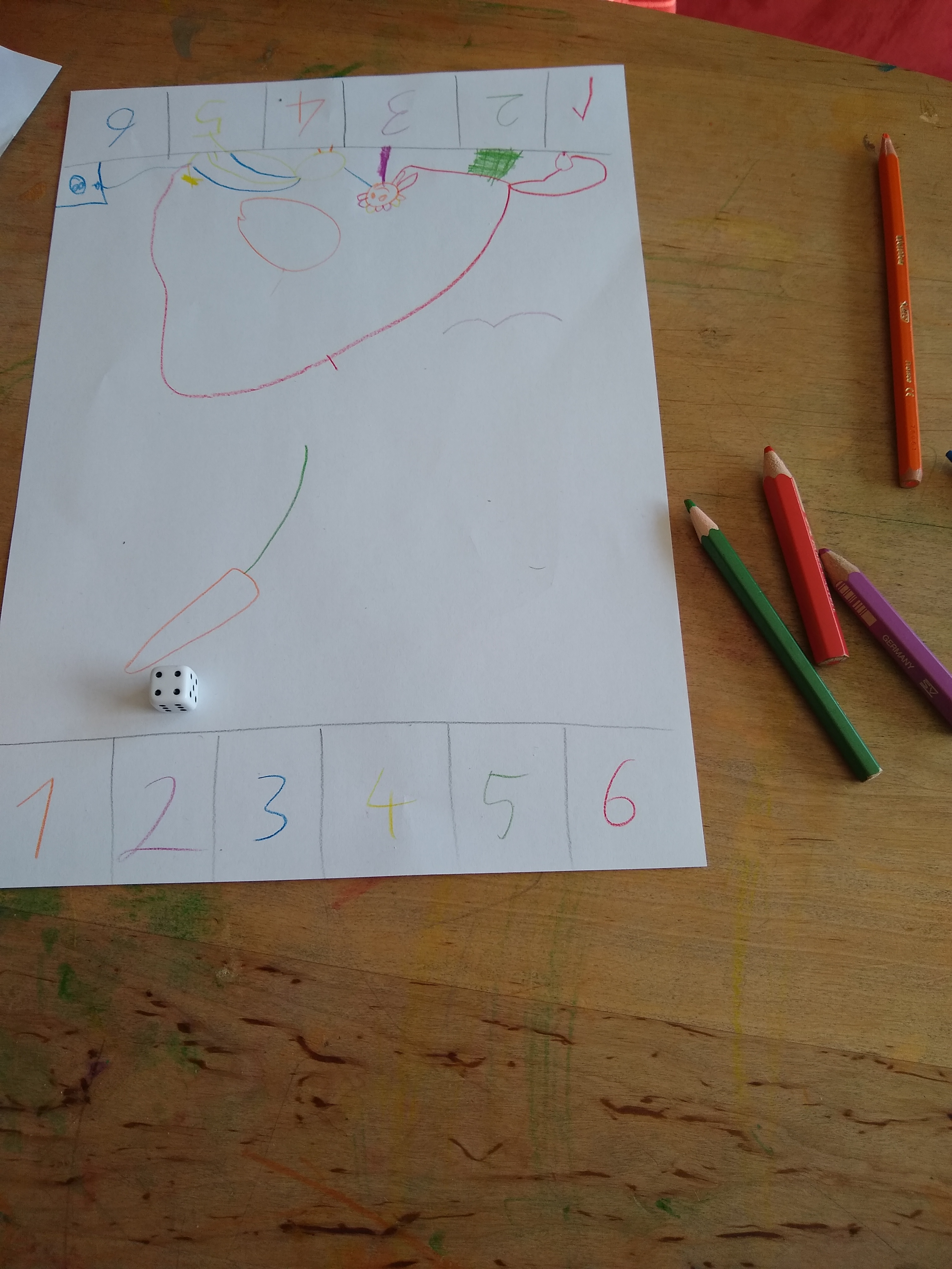 One page lying on a wooden table with numerals 1 to 6 drawn in six different
colors on each short side and, in the middle of the page, various drawings
consisting of strokes in one of the six colors. On the page lies a six sided
dice. Next to the page, three colored pencils are
visible.